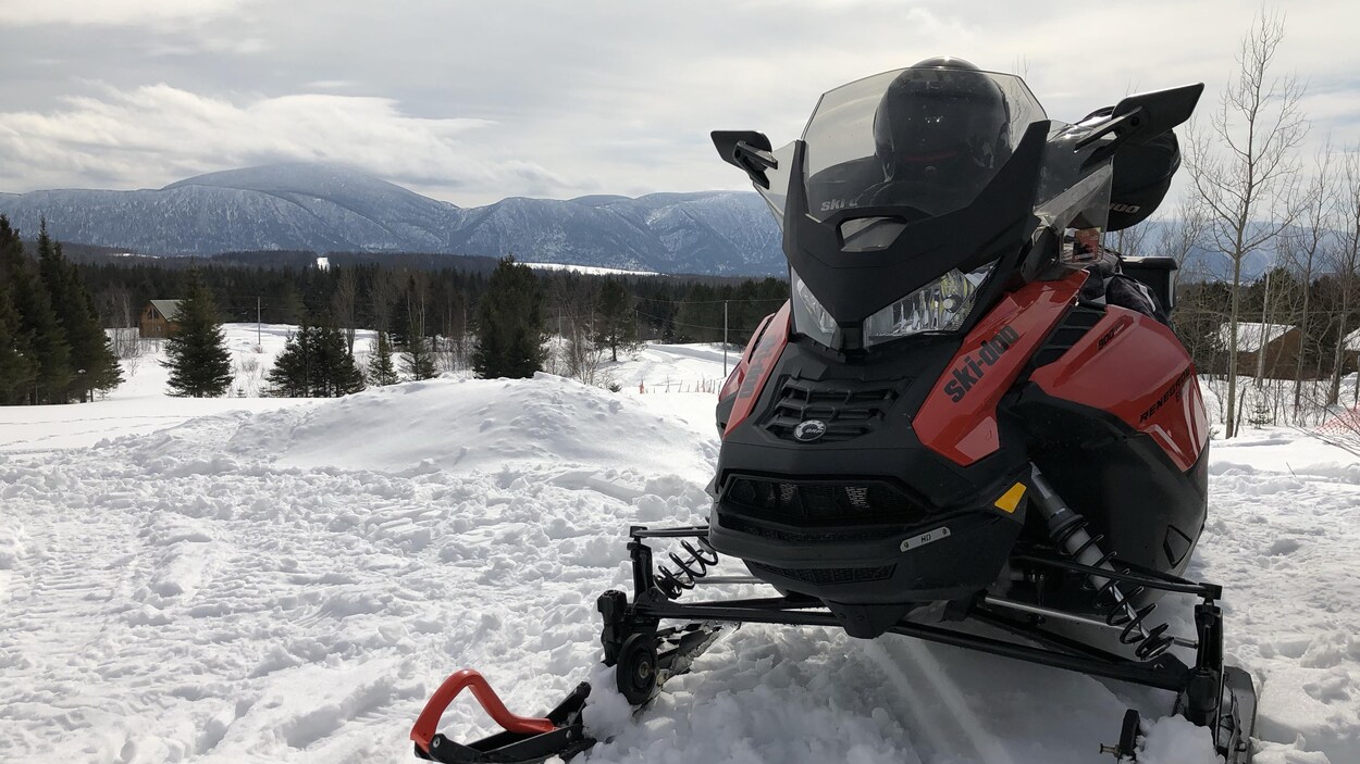 Motoneigiste à l'avant-plan, montagnes magnifiques derrière.