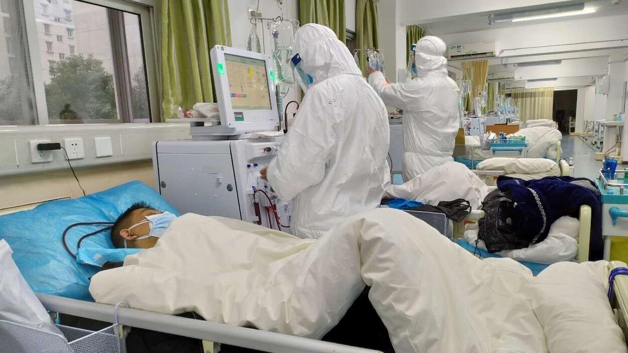 Un patient alité avec deux travailleurs de la santé qui portent des uniformes de protection.