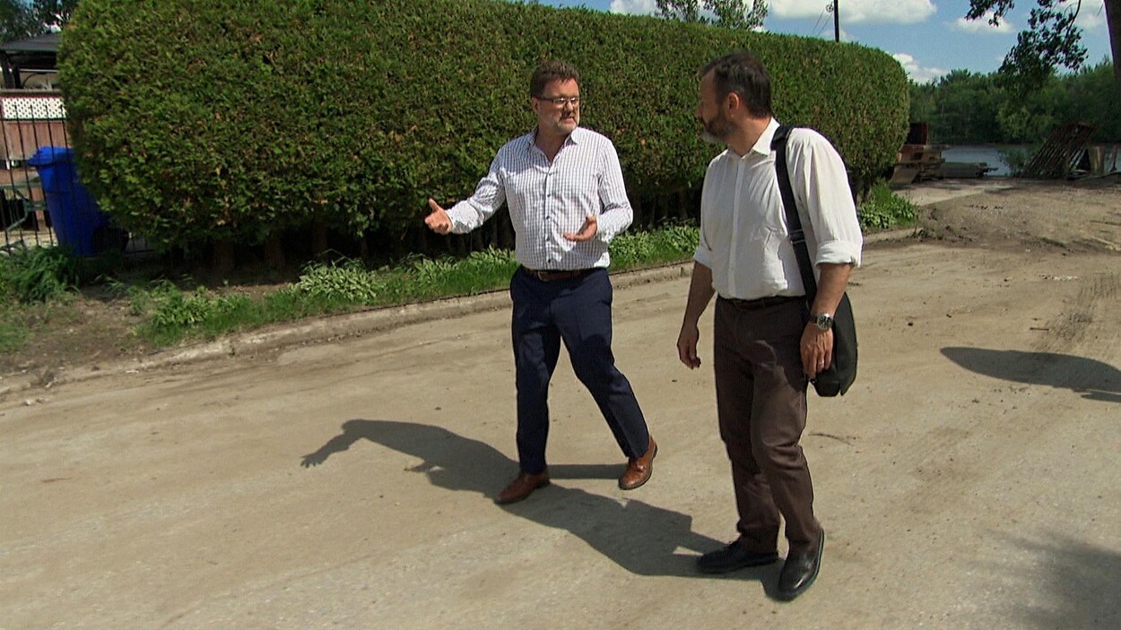 Les deux hommes marchent dans une rue longeant un cours d'eau.