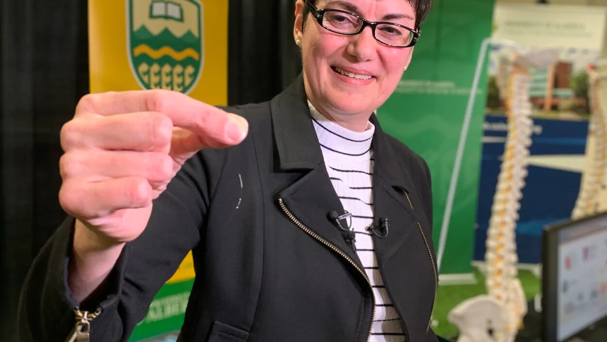 Une femme tient un implant entre les doigts.