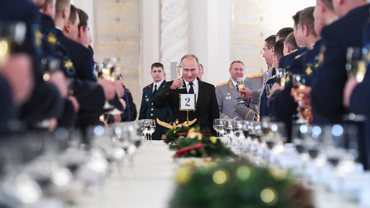 Le président Poutine, au bout d'une longue table rectangulaire, lève son verre en l'honneur de militaires russes.