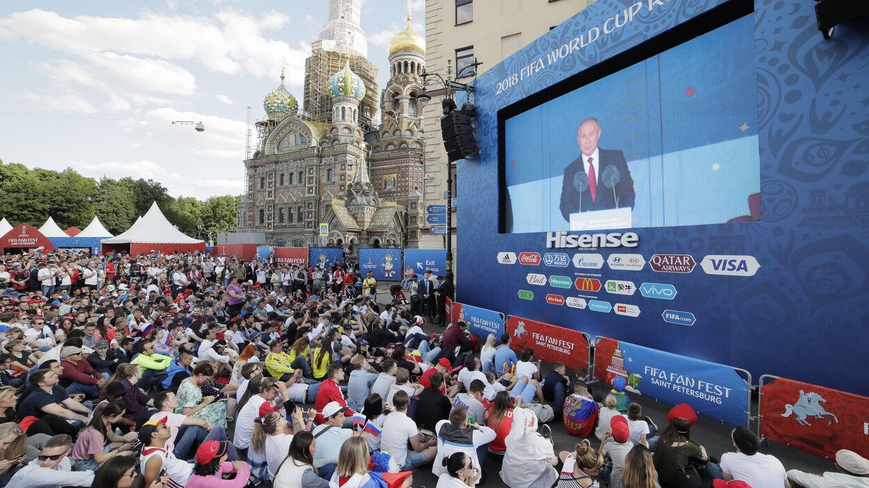 Des gens regardent le discours du président russe Vladimir Poutine avant le match inaugural de la Coupe du monde. Des gens regardent le discours du président russe Vladimir Poutine avant le match inaugural de la Coupe du monde.