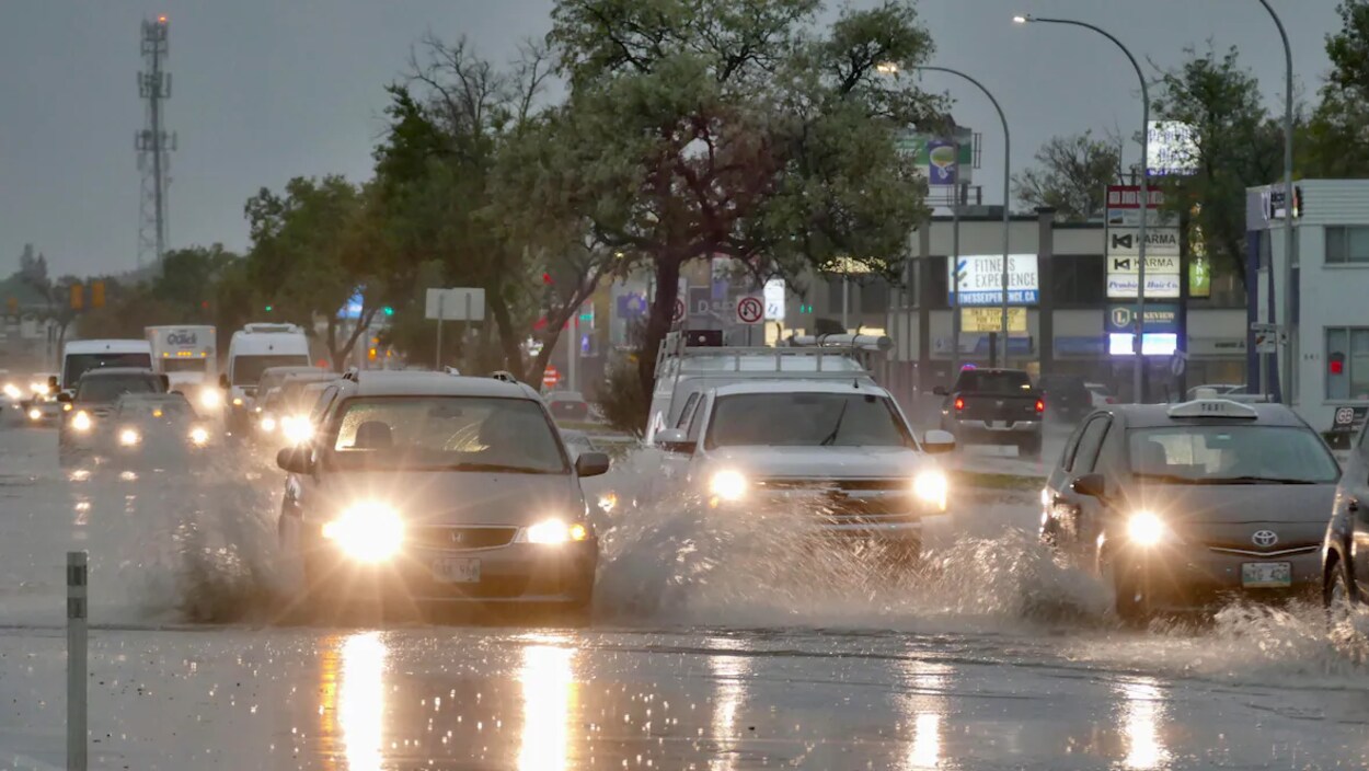 Des voitures roulent sur une rue où une bonne quantité d'eau s'est accumulée.