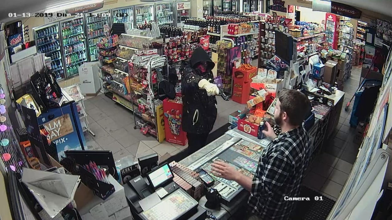 Dans un dépanneur, un homme cagoulé dans un dépanneur pointe une arme à feu en direction.