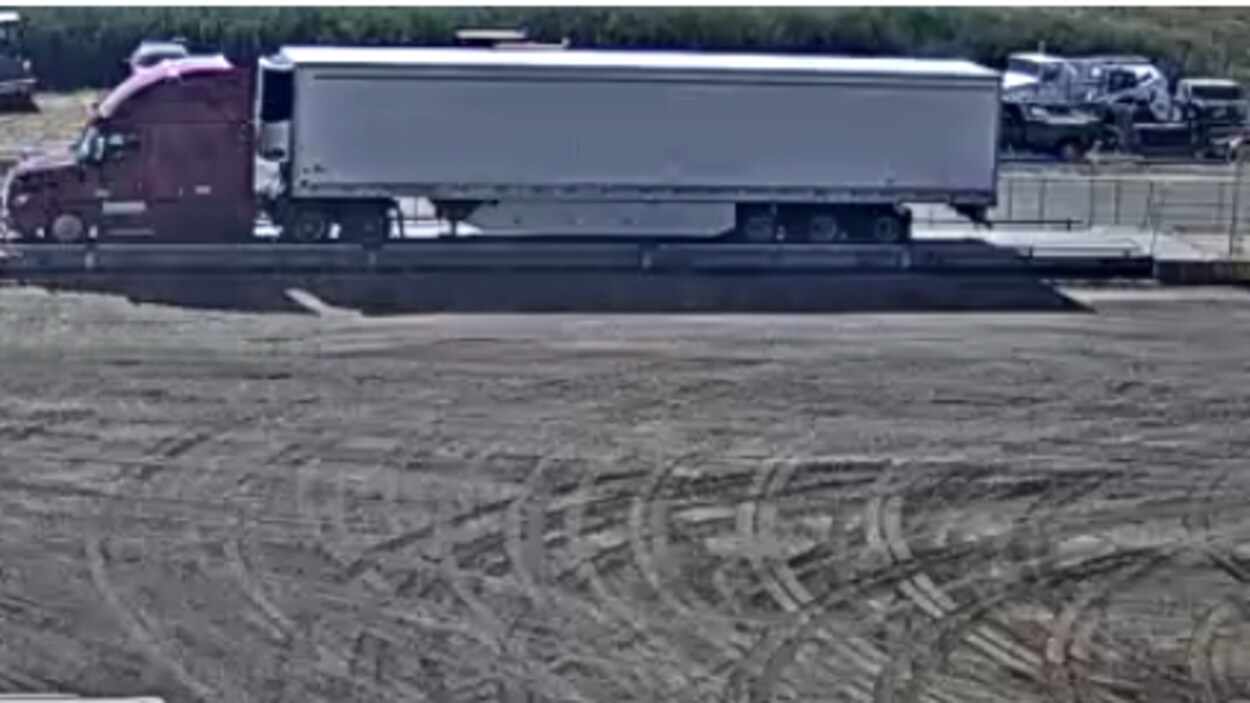 Un camion bordeaux avec une remorque blanche sur une image de vidéo de surveillance.