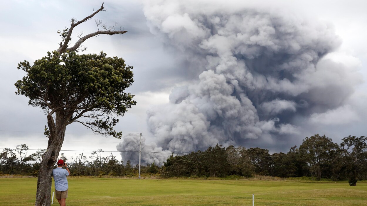 Un homme regarde au loin les éruptions du volcan Kilauea, qui assombrit le ciel de fumée.