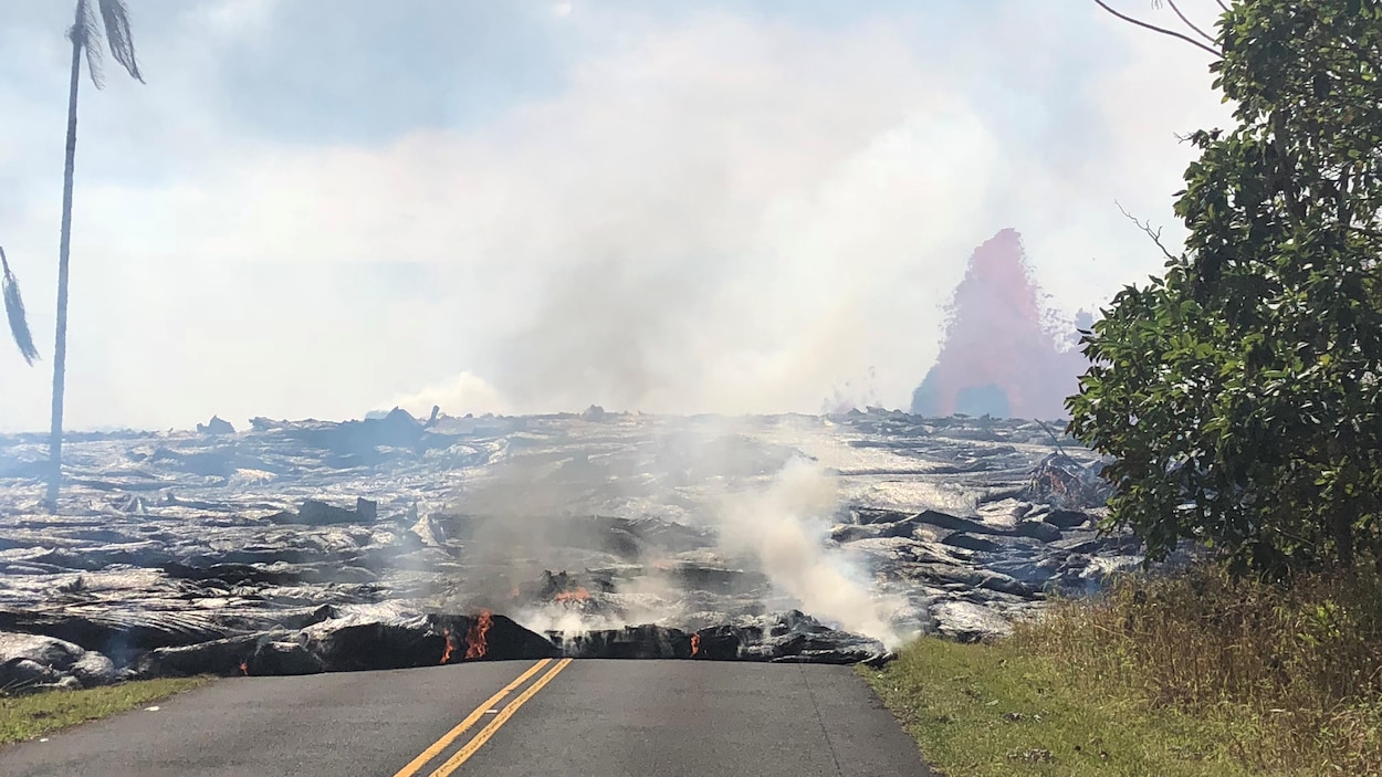De la lave se répand sur l'avenue Leilani, alors qu'au loin on aperçoit une fontaine de lave qui jaillit du volcan Kilauea.