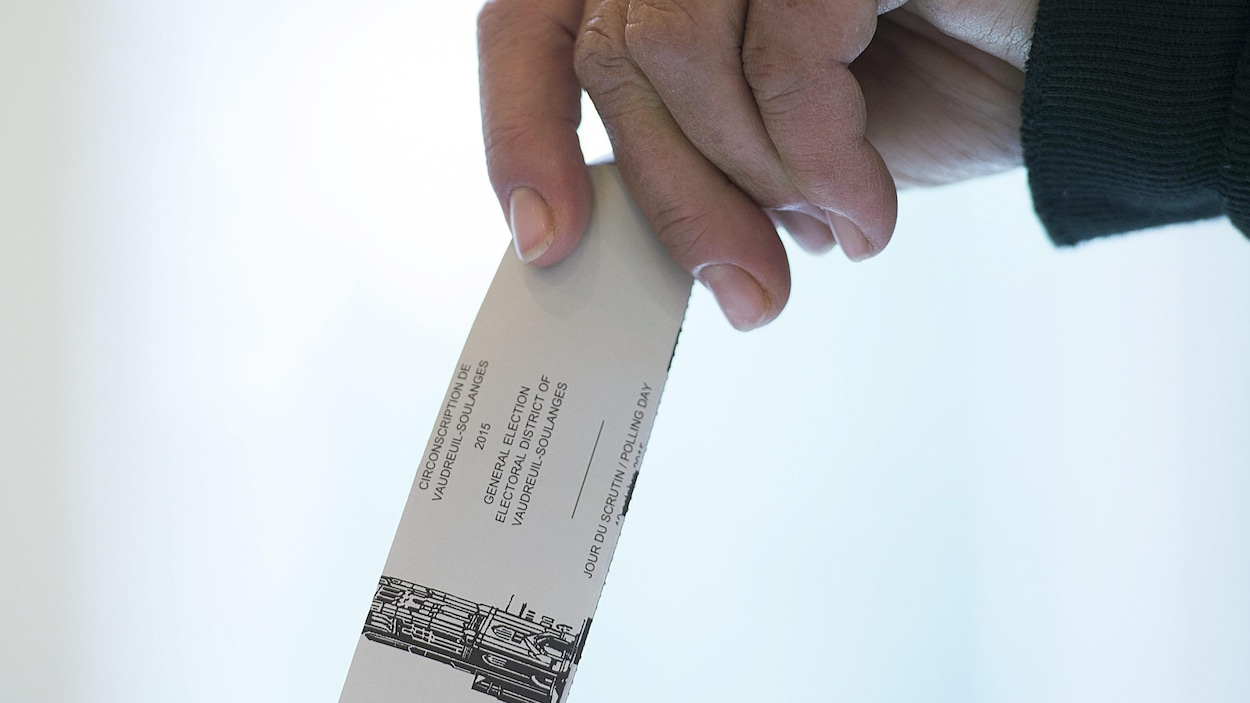Une personne tient un bulletin de vote pour le déposer dans l'urne.