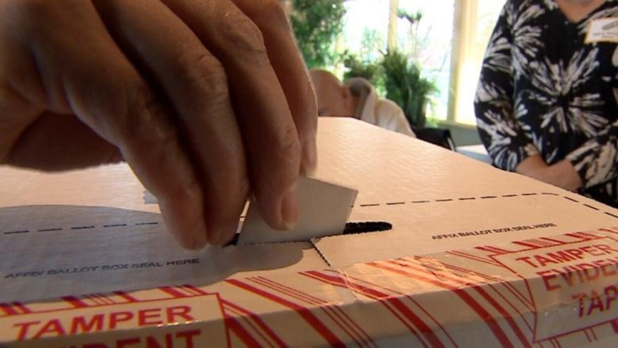Une main glisse un bulletin de vote dans une urne.