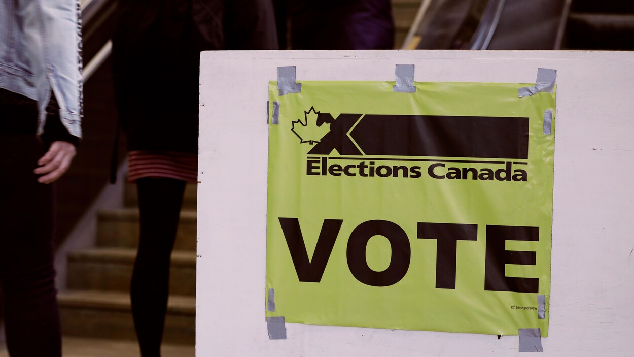 Une affiche identifiant l’emplacement du bureau de vote. On aperçoit, en arrière-plan, des électeurs.