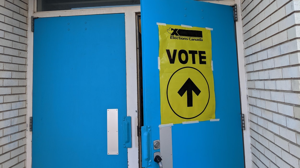 Gros plan sur une porte extérieure bleue entrouverte et sur laquelle est apposée une affiche jaune sur laquelle on peut lire Élections Canada Vote.