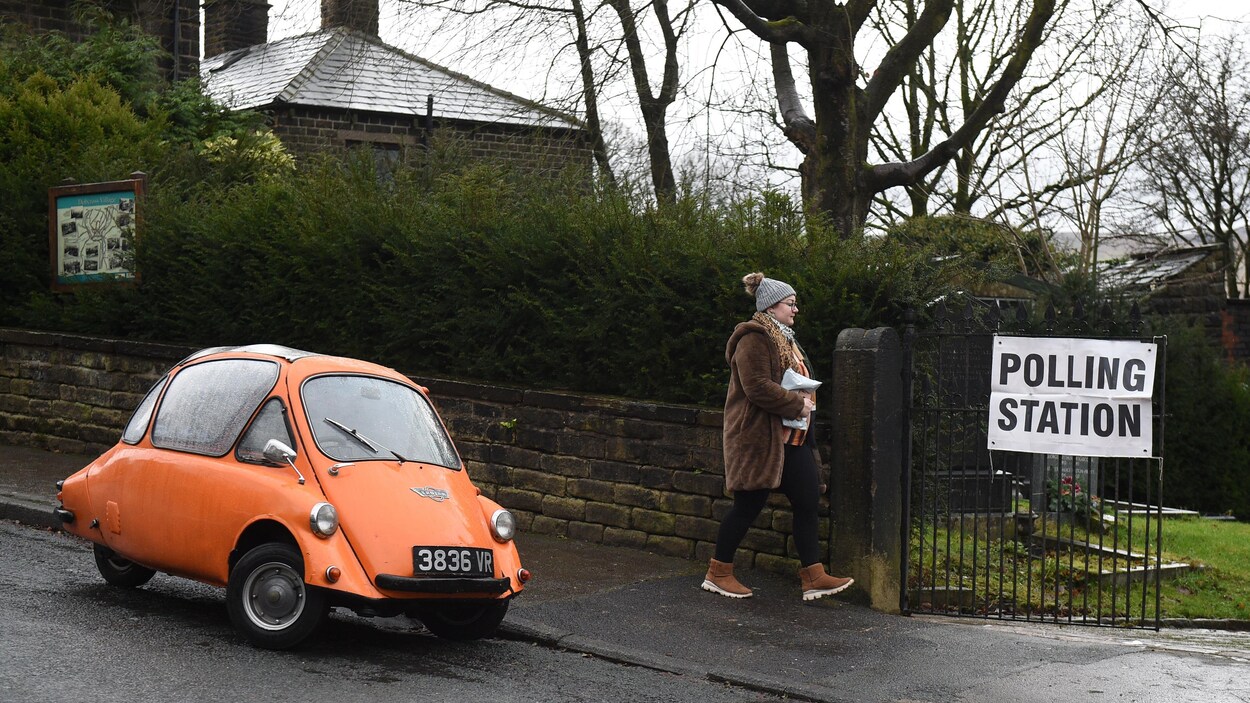 Une femme marche près d'une voiture à trois roues.