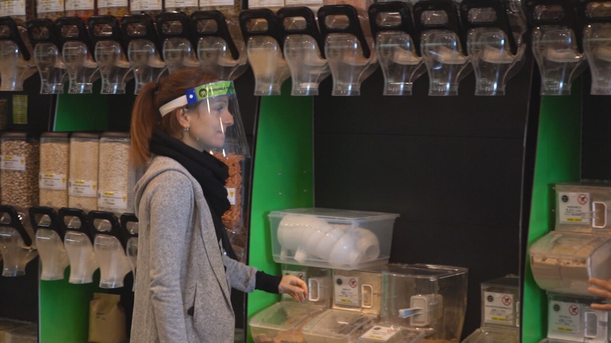 Une employée porte une visière de protection devant un étalage de produits en vrac.
