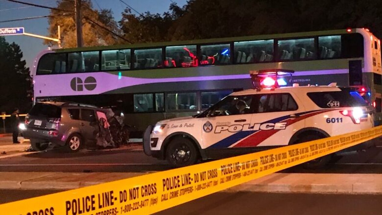Le VUS au capot embouti à côté d'un autobus GO et d'un véhicule de police.