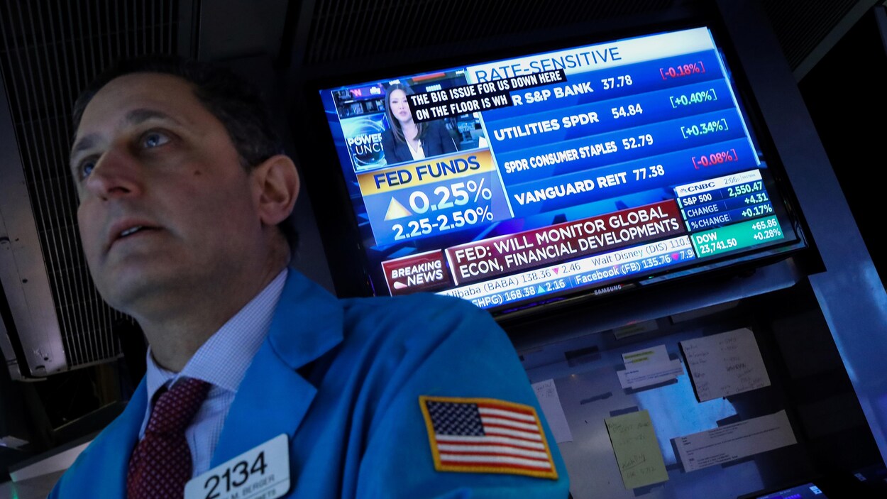 Un employé de Wall Street travaille tandis qu'une télé derrière lui affiche l'annonce de la Fed.