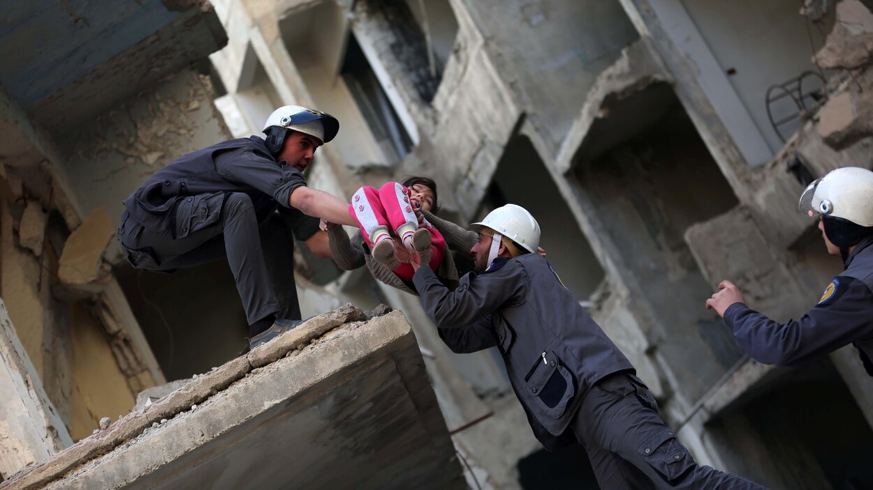 Trois hommes habillés de gris et portant des casques blancs secourent une petite fille habillée de rose des décombres, lors d'un exercice.