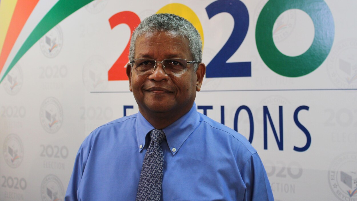 Wavel Ramkalawan pose, souriant, devant une affiche électorale.