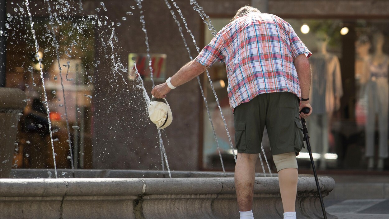 Un homme avec un chapeau dans les mains près d'une fontaine.