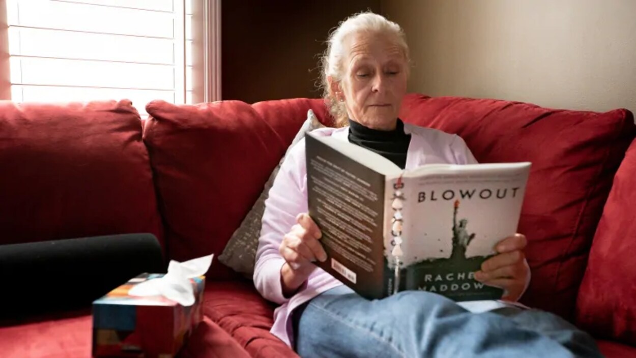 Une femme assise sur un sofa rouge lisant un livre.