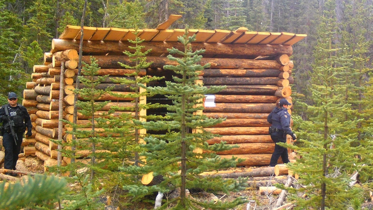 Deux agents patrouillent autour d'une petite loge en bois rond.