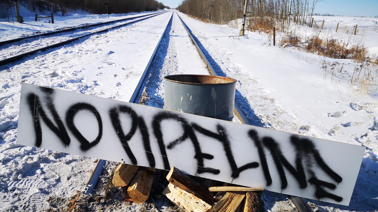 Plan serré d'un barrage sur un chemin de fer où une affiche indique en anglais : « pas de pipeline ».
