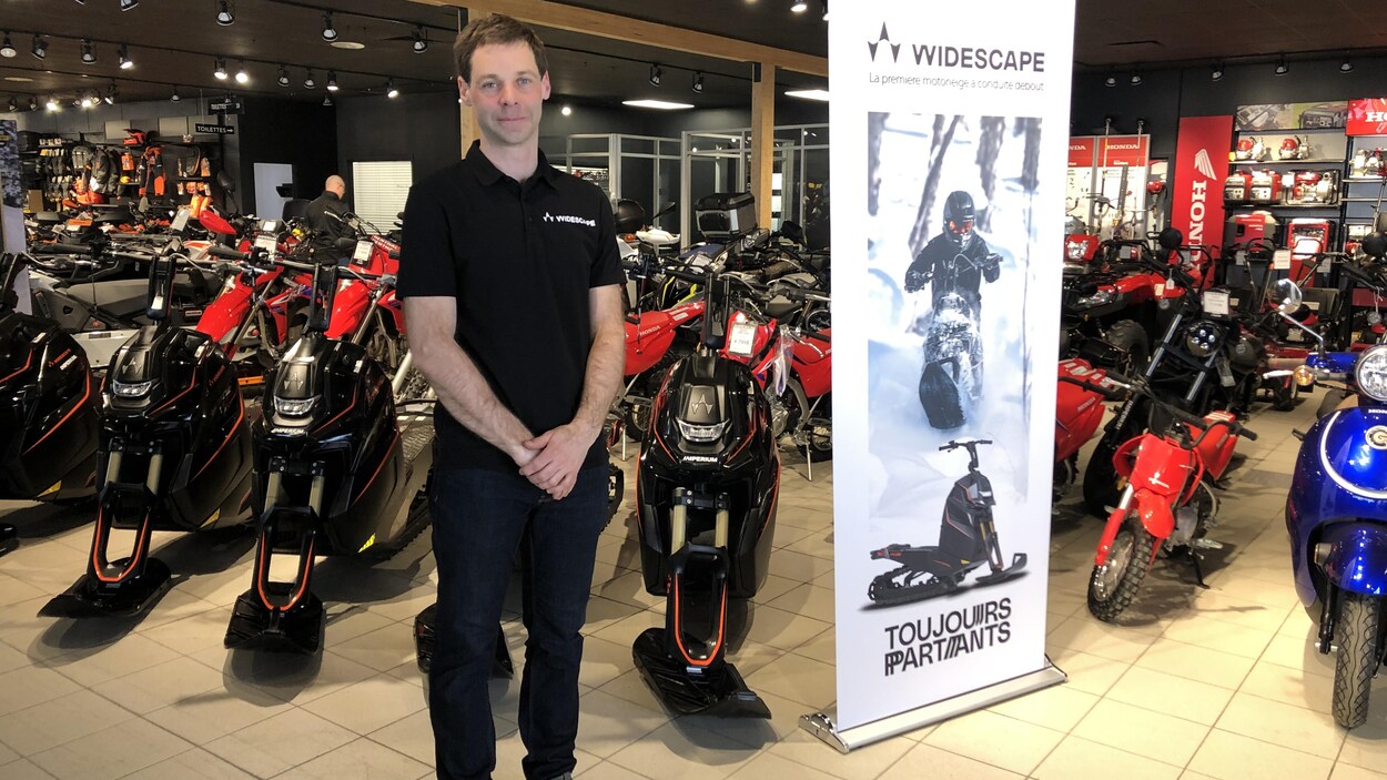 Un homme se tient devant des motoneiges debout dans un commerce.