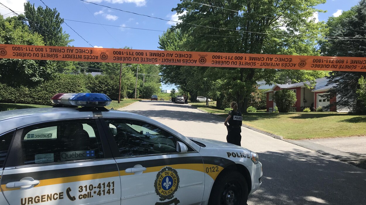 Une voiture de la Sûreté du Québec et une policière devant une rue bloquée par du ruban orange.