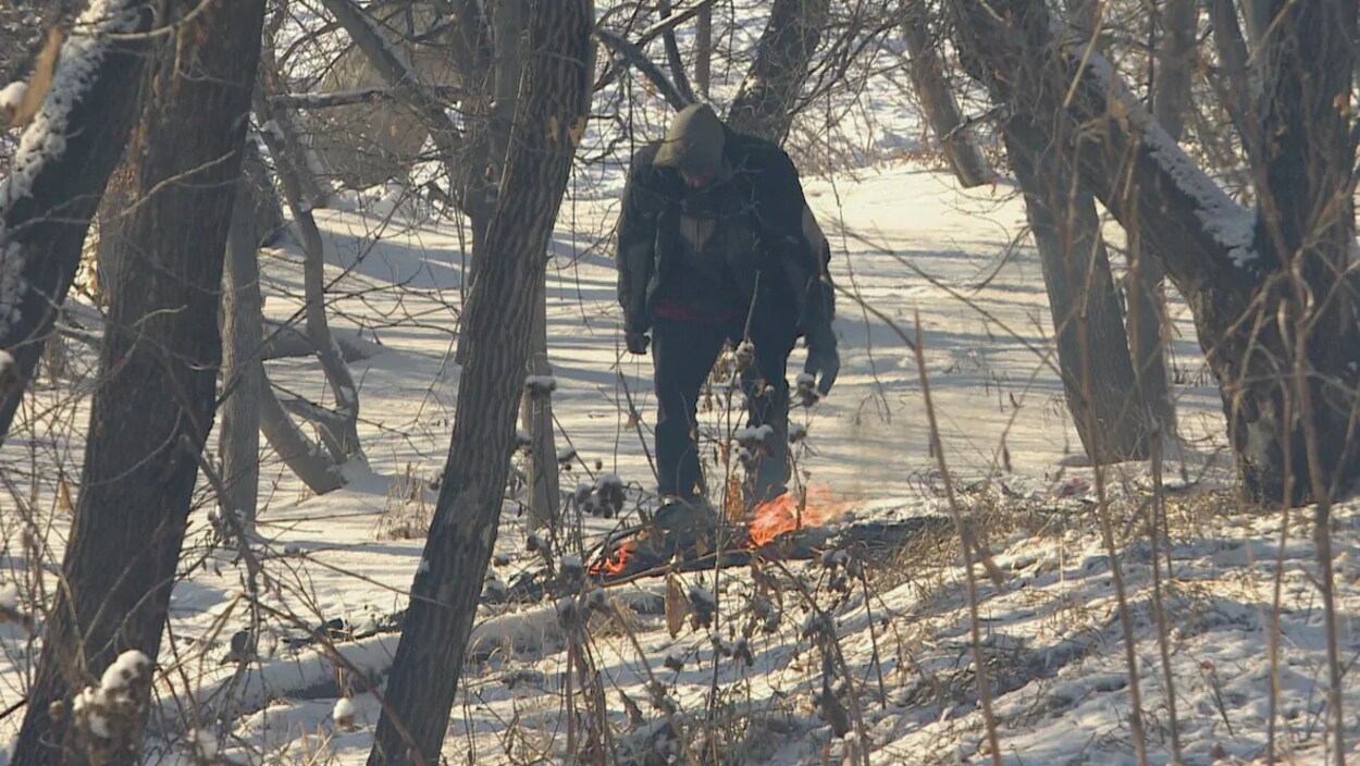 Un homme au milieu d'arbres et devant un feu dans la neige.