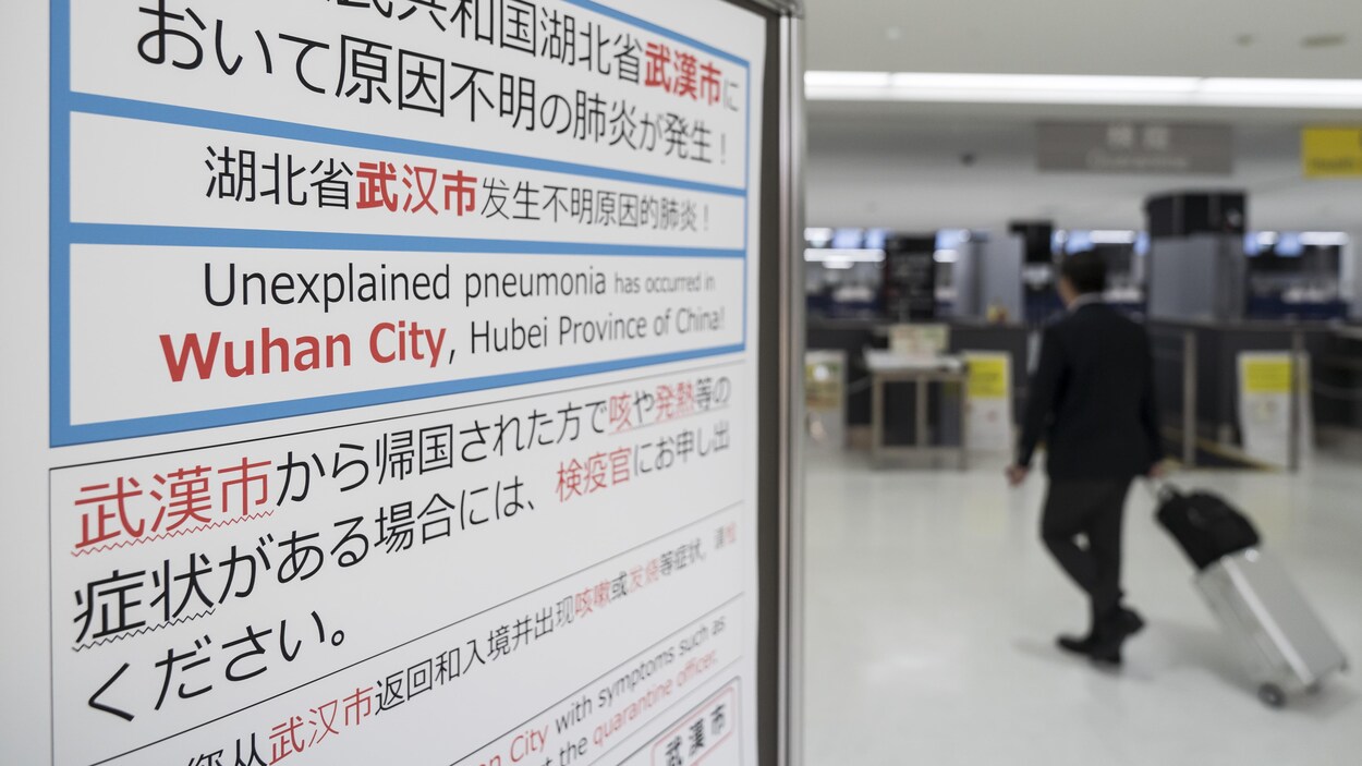 Un voyageur passe près d'une affiche écrite en anglais et en mandarin qui demande aux gens de déclarer leurs symptômes s'ils sont grippés.