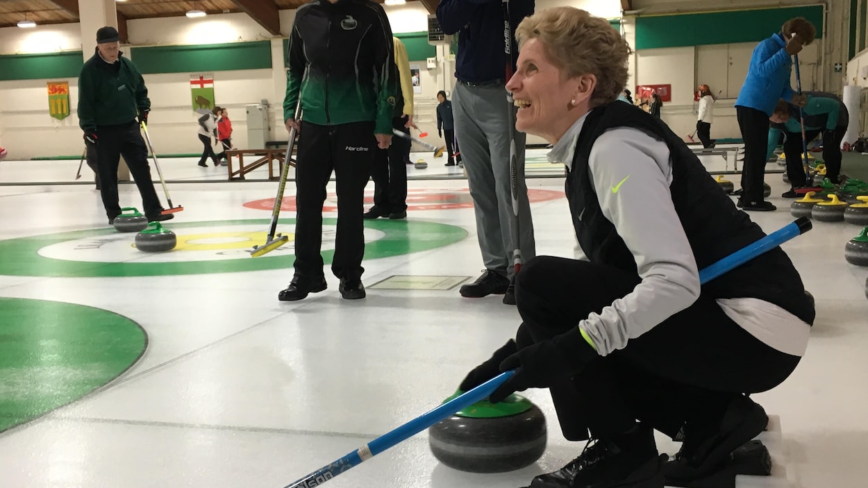 Photo de Kathleen Wynne penchée sur la glace qui tient une pierre de curling. Photo de Kathleen Wynne penchée sur la glace qui tient une pierre de curling.
