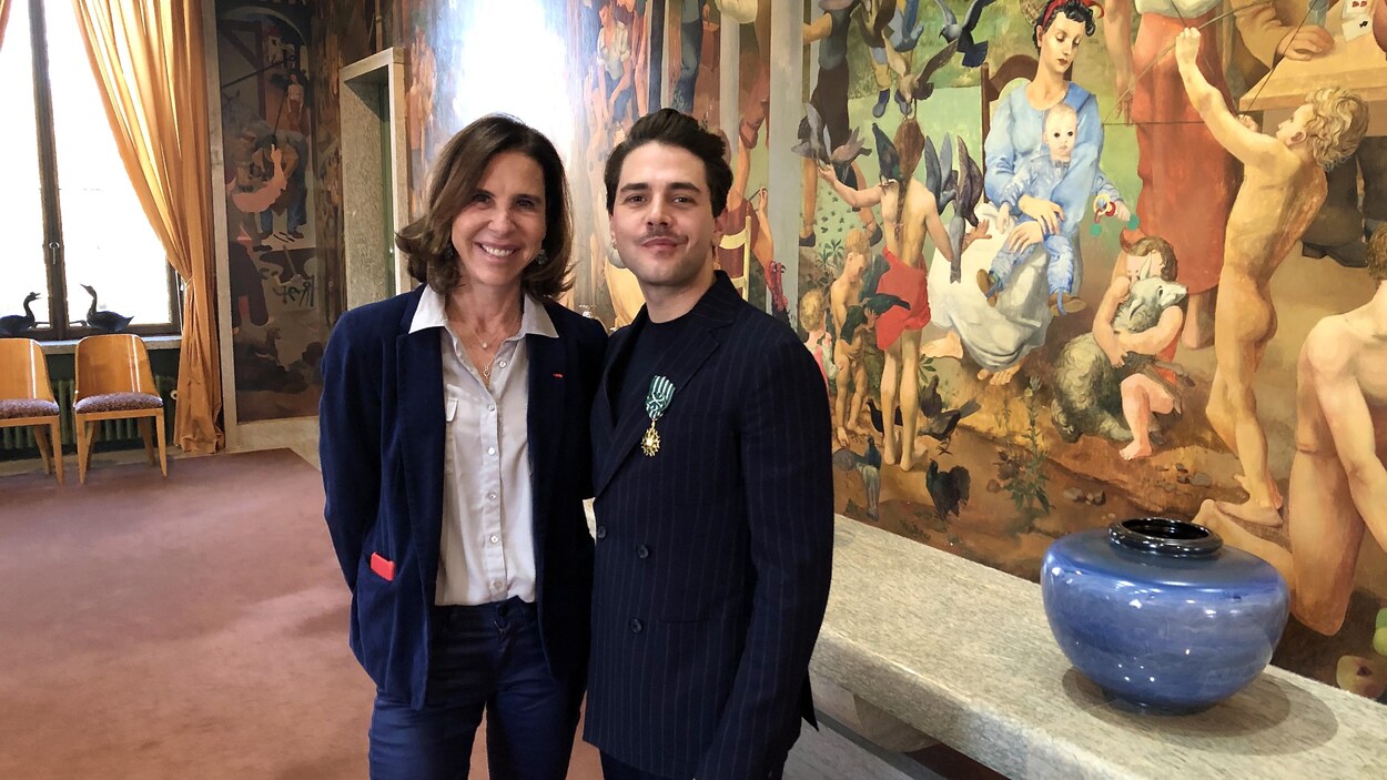 Xavier Dolan porte son insigne épinglé sur un costume noir aux rayures blanches et Kareen Rispal est vêtue d'une chemise claire et d'une veste sombre.