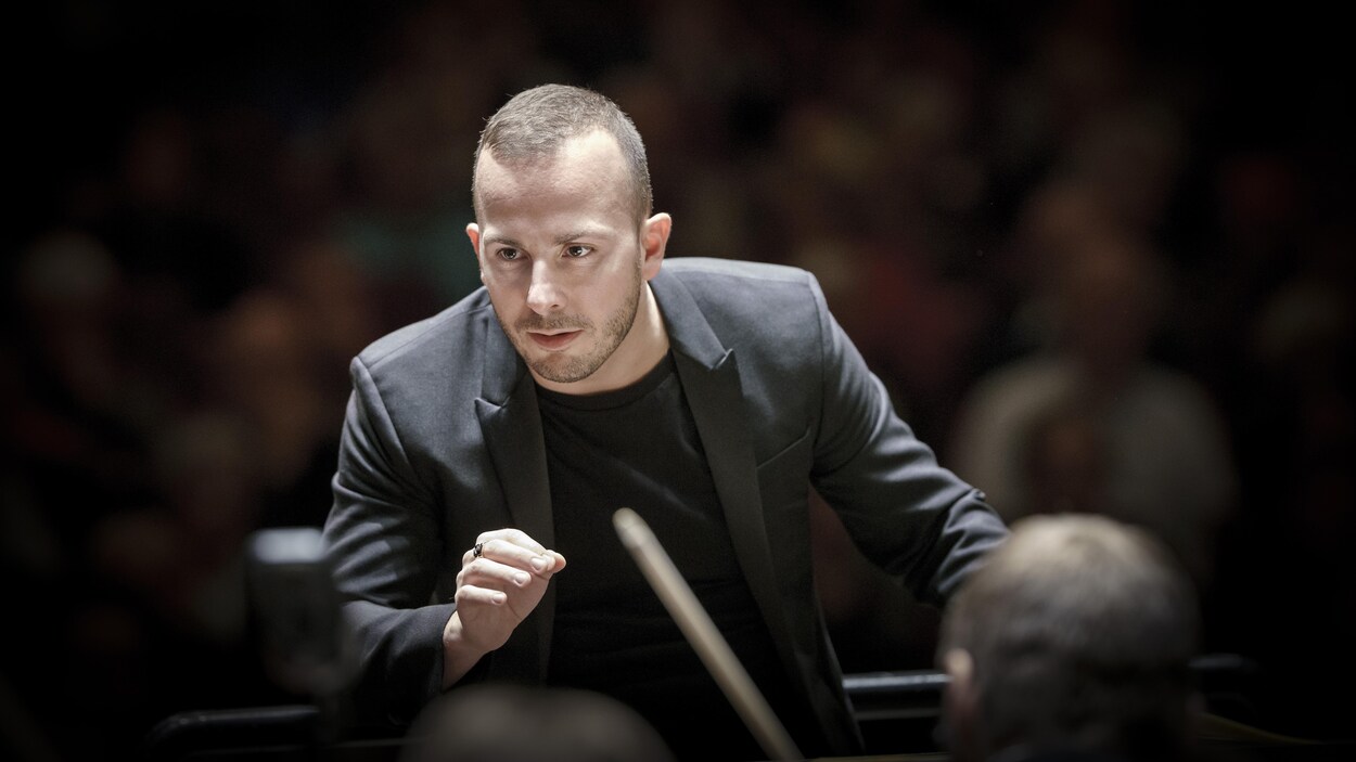 Le regard concentré, le chef d'orchestre dirige à la main son ensemble.