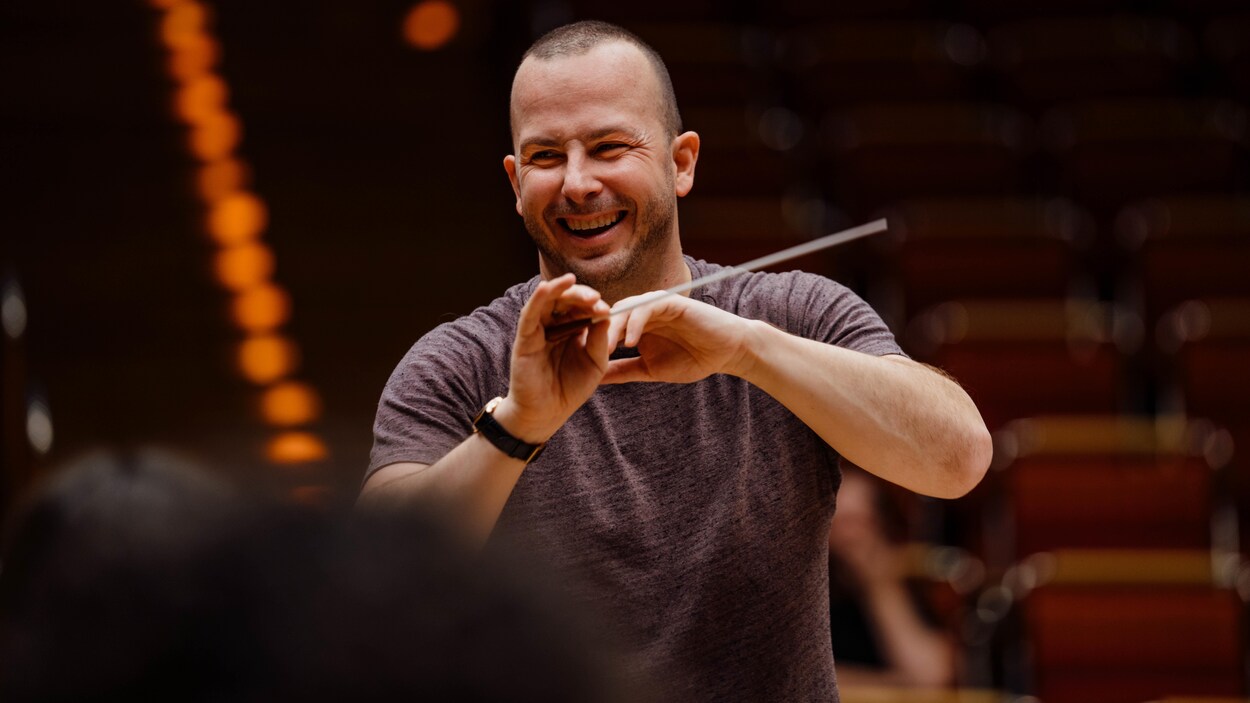 L'homme sourit alors qu'il tient une baguette de chef d'orchestre dans sa main.