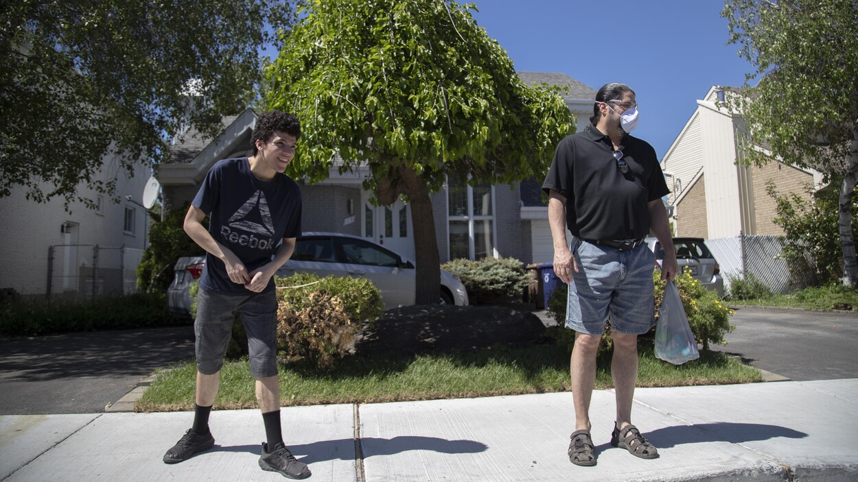 Yanny et Jacques Mignault, qui porte un masque, se tiennent à distance, sur le trottoir d'un quartier résidentiel.