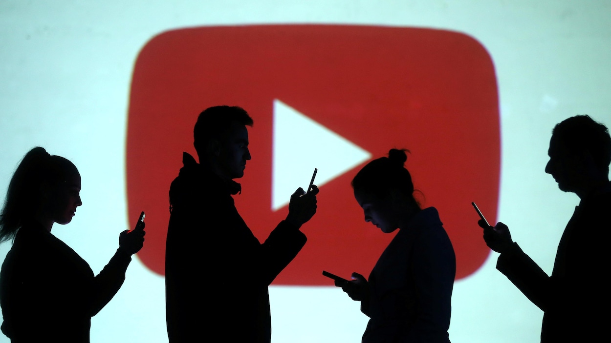 Des silhouettes regardent des téléphones devant un arrière-plan du logo de YouTube.