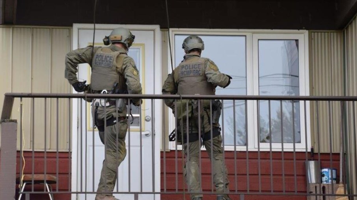 Deux policiers en uniformes de combat sont sur un balcon devant la porte d'un appartement.