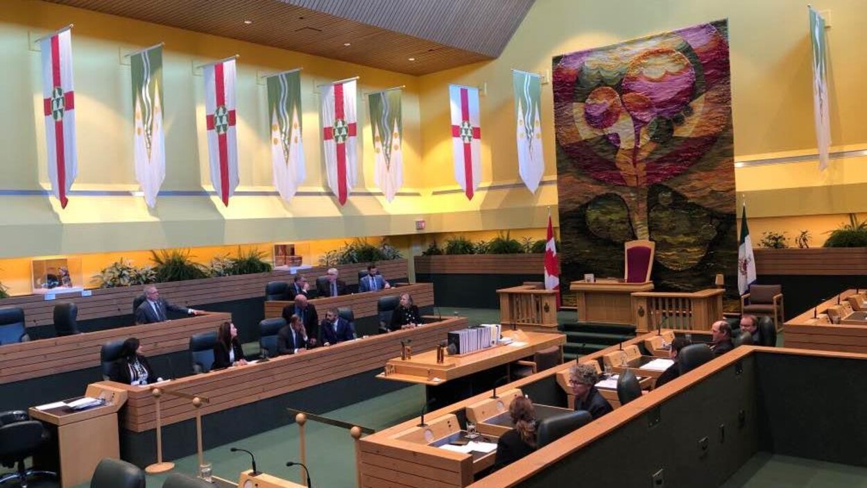 Des gens assis dans une grande salle entourée de drapeaux.