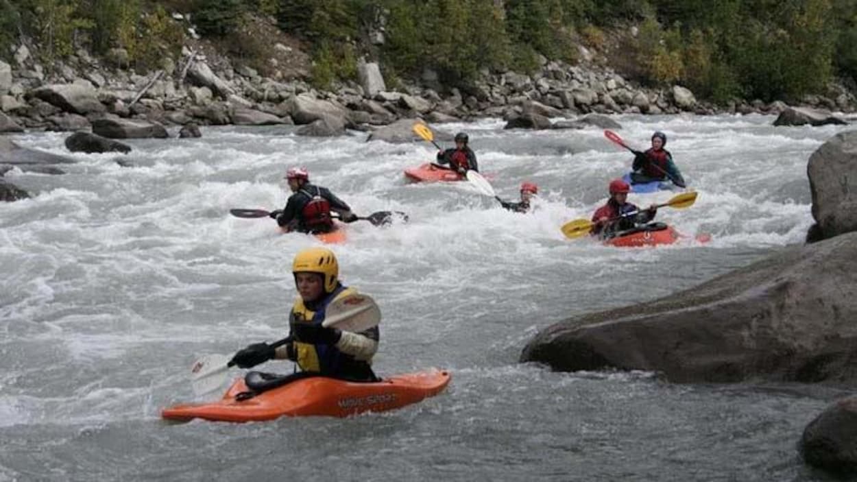Des jeunes en kayak pagaient dans des rapides sur un cours d'eau.