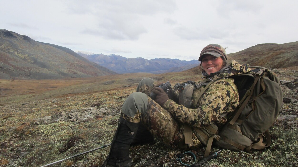 Maya Poirier dans les montagnes avec des jumelles à la main sourit à la caméra.
