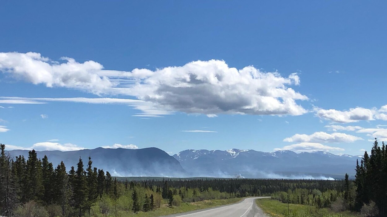 Photo prise le long d'une route avec de la fumée au loin devant des montagnes.