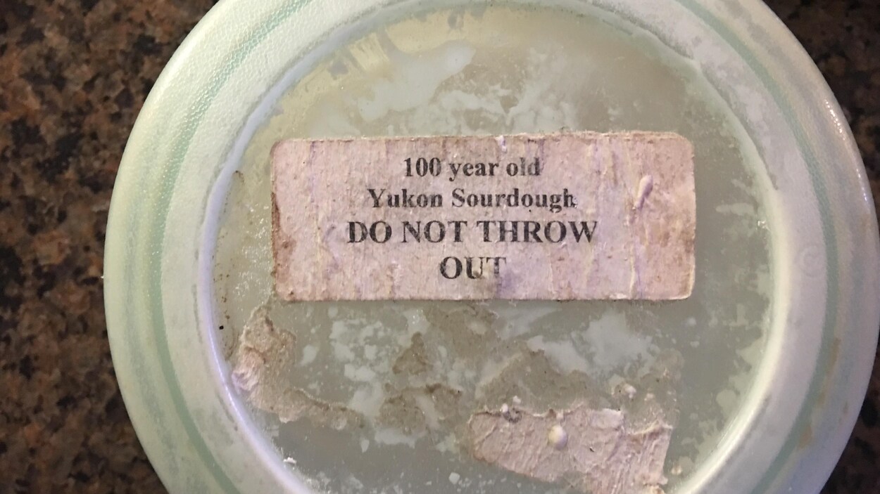 Le couvercle du récipient contenant le levain avec une étiquette indiquant qu'il s'agit d'un levain de 100 ans qu'il ne faut pas jeter.