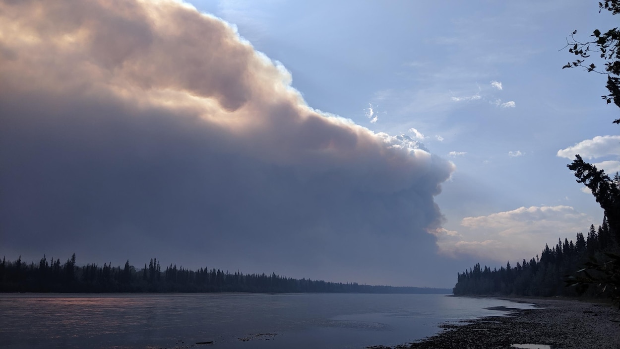 Fumée épaisse dans le ciel au-dessus d'un cours d'eau.