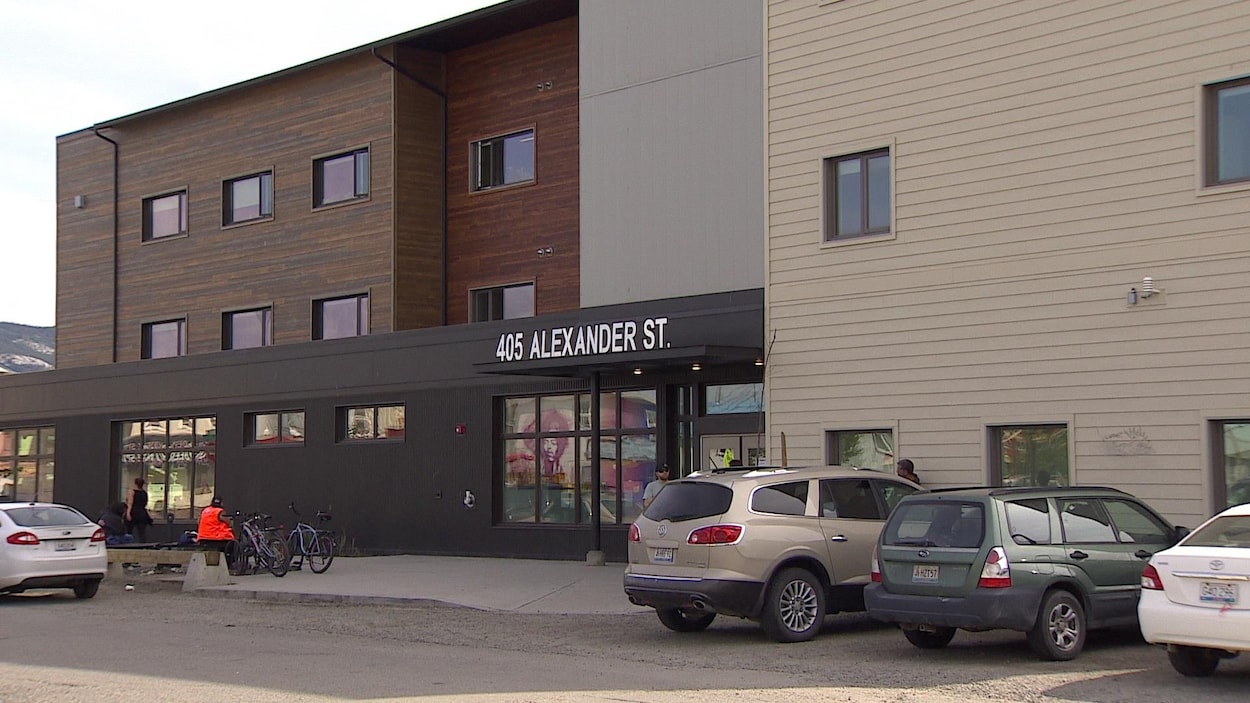 Des voitures stationnées et des gens assis sur un banc devant un bâtiment.