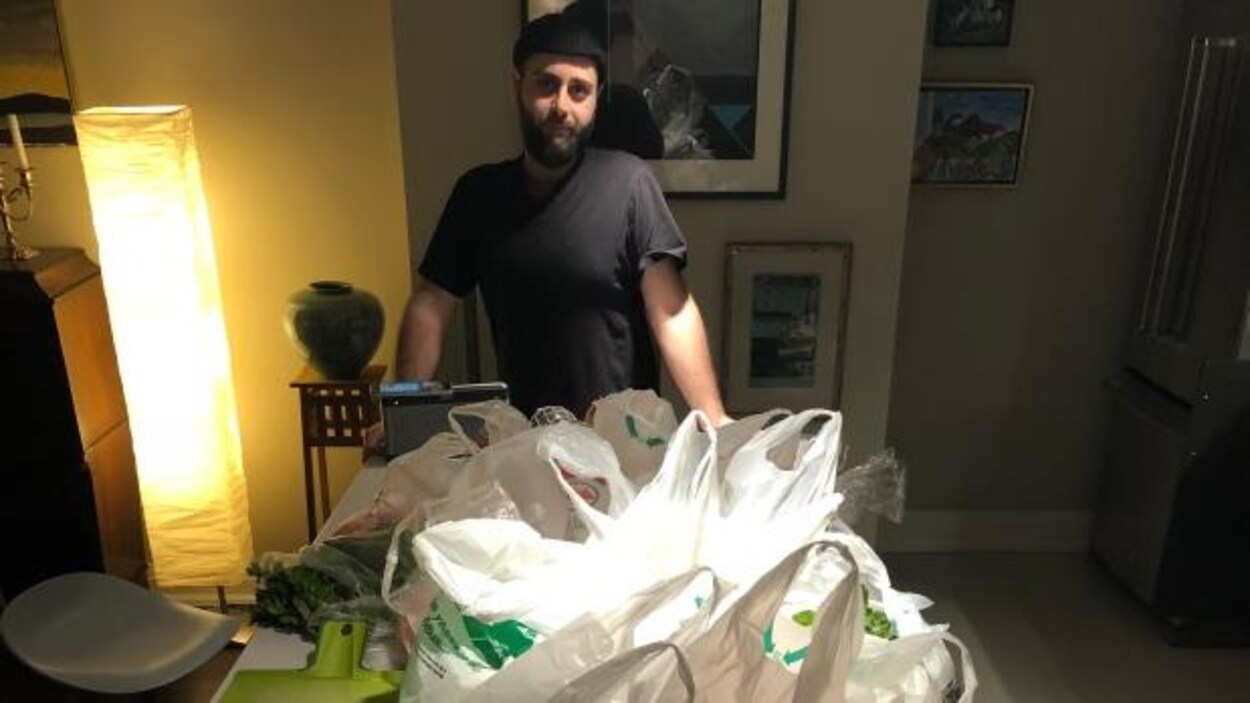 Yusuf Celik devant une table avec des sacs de course.