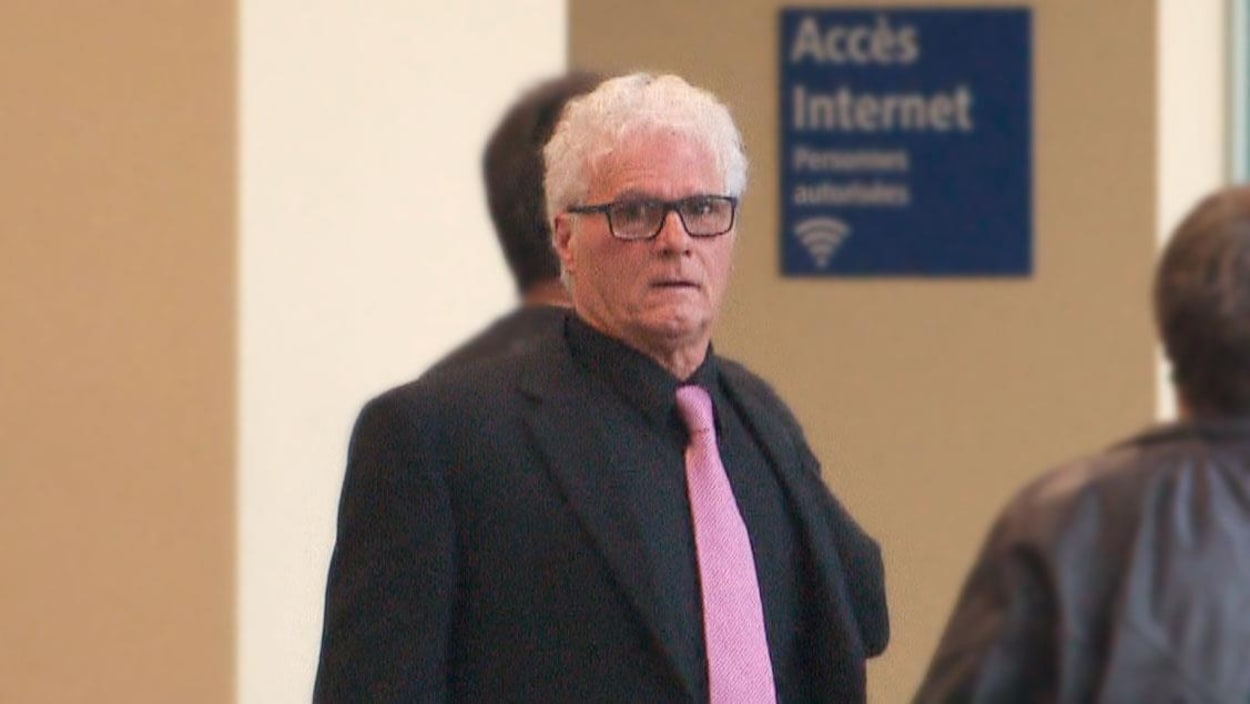 Yves Colosse Plamondon, un homme aux cheveux blancs, regarde la caméra. Il porte une cravate rose et un complet noir.
