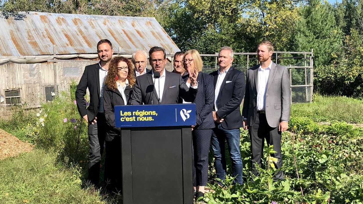 Les huit intervenants sont réunis derrière un lutrin, dans un jardin.