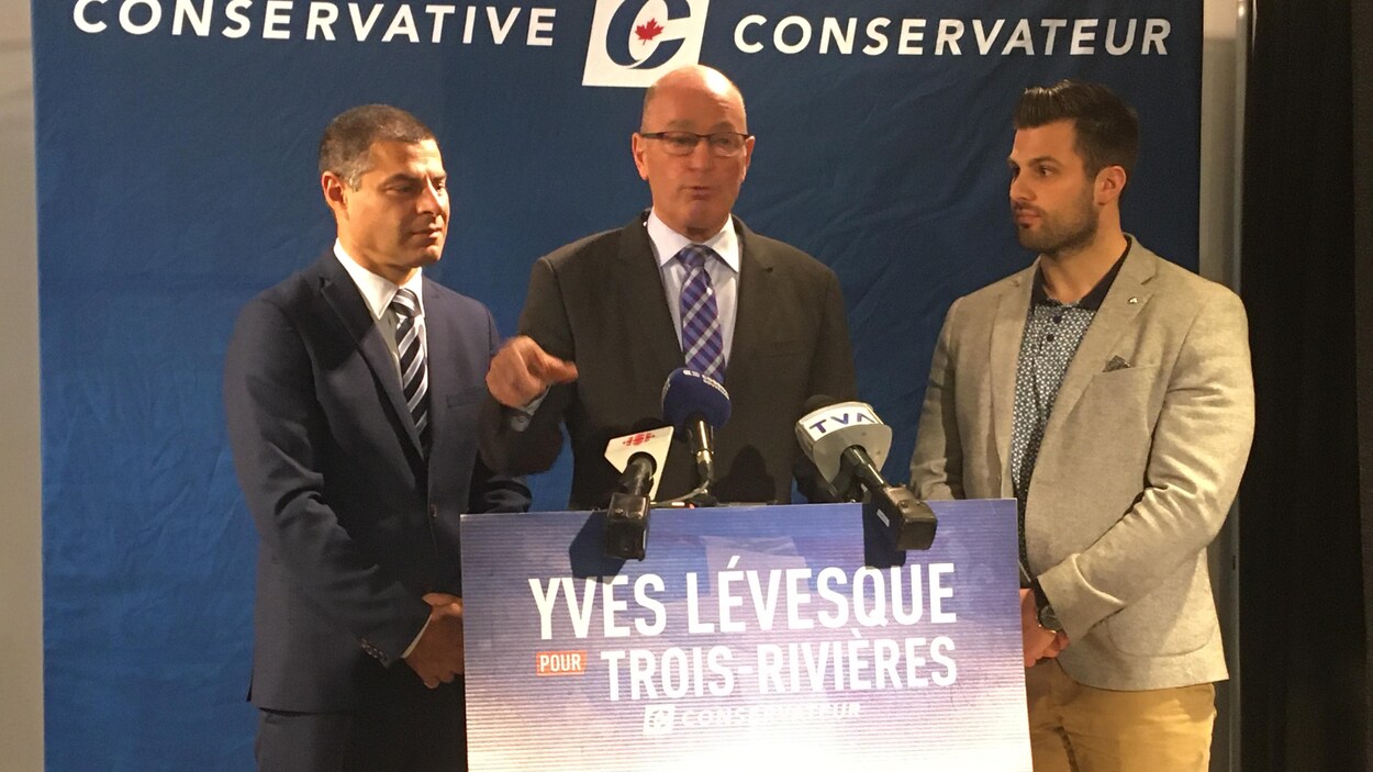 Yves Lévesque derrière un lutrin qui parle. Alain Rayes est à sa droite.