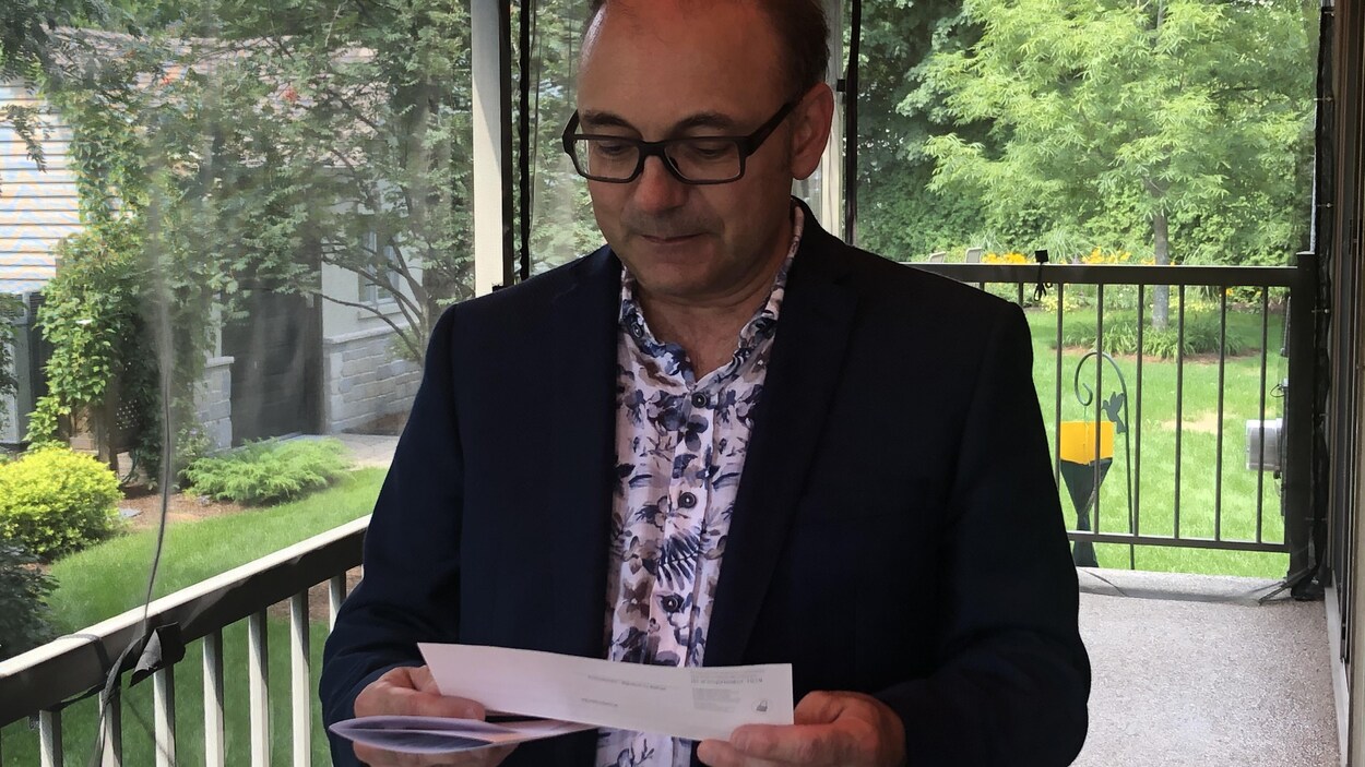 Yvon Boivin tient dans ses mains un chèque qu'il attend depuis 2009. Il est dans sa cour arrière.