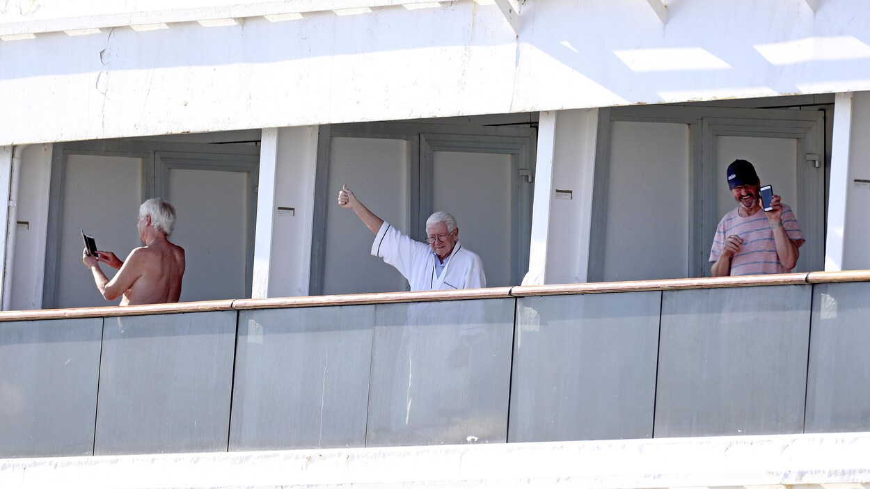 Un homme en robe de chambre lève le pouce en l'air depuis le pont du navire.
