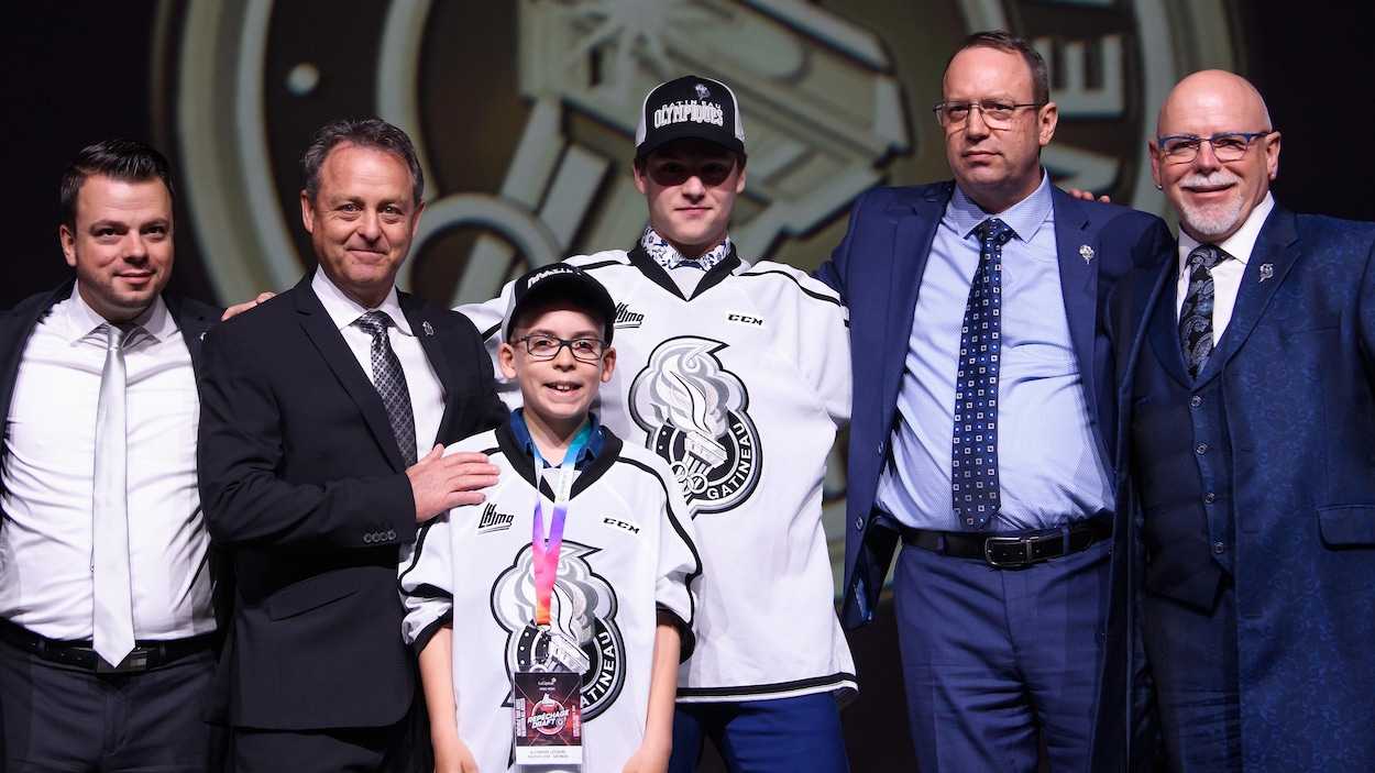 Un jeune joueur de hockey vêtu de son chandail pose fièrement après avoir été repêché dans la LHJMQ.